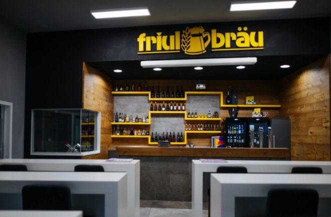 Aula della FRB Academy con i banchi e la parete bar in legno con l’insegna Friulbräu