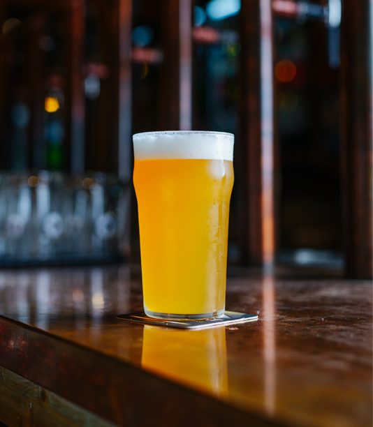 Pinta di birra chiara sul bancone, bar sullo sfondo