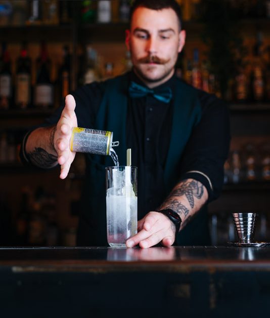 Barman che versa l’acqua tonica in un bicchiere con ghiaccio
