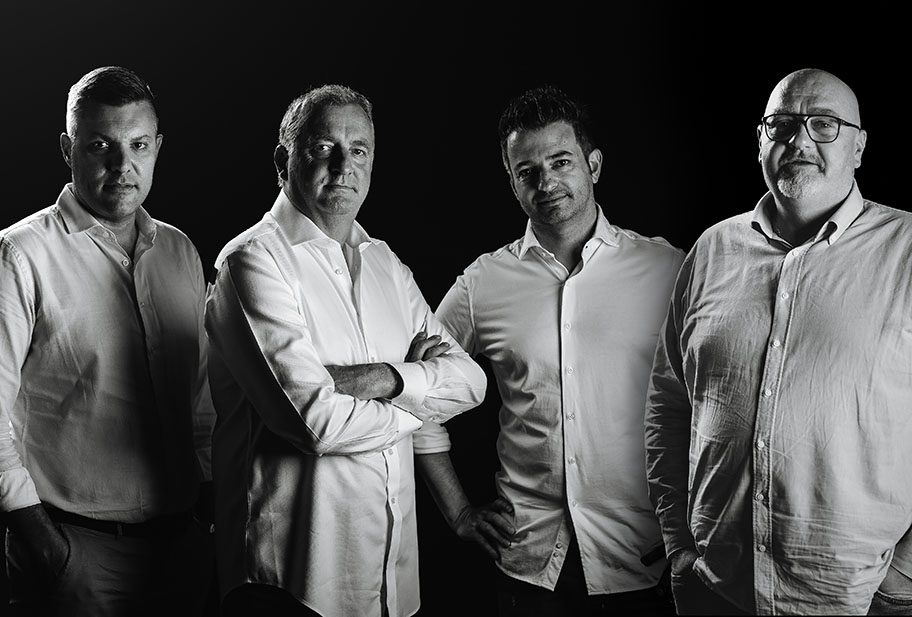 Quattro uomini in camicia bianca a braccia conserte, ritratto in bianco e nero