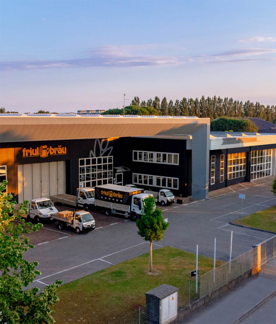 Sede nera con l’insegna gialla Friulbräu e i camion col marchio, al tramonto